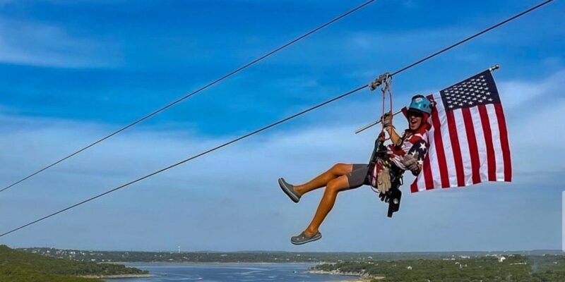 Zipliner holding American Flag while zipping over the lake.